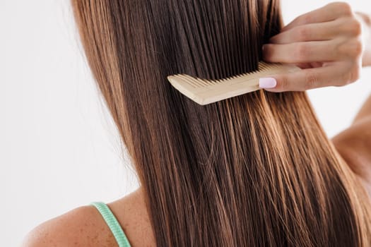 A person combing their long, straight brown hair with a wooden comb. hair care, hair problem