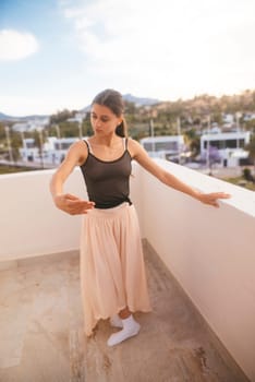 A graceful and skilled dancer beautifully showcases a ballet pose on a stunning balcony with a picturesque background