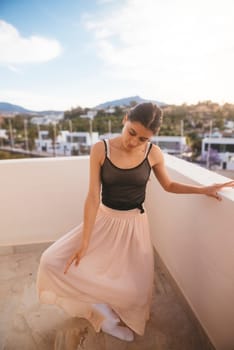 A graceful woman poses elegantly in a beautiful flowing skirt, savoring a serene sunset view from her balcony