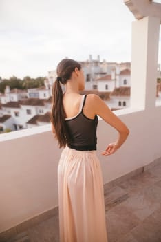 A stylish woman wearing a chic black top paired with a flowing skirt enjoys the captivating view from her balcony