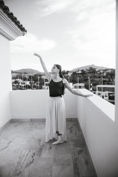 A talented dancer in elegantly flowy attire strikes a beautifully poised pose on a scenic, picturesque balcony