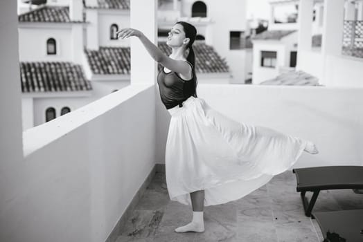 A graceful ballerina showcases her artistry on a sunlit balcony, captured in timeless black and white.