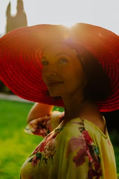 Portrait of a woman wearing a large red sun hat during golden hour. The soft, warm sunlight highlights the edges of the hat and casts a beautiful glow on her face, creating a serene and tranquil atmosphere