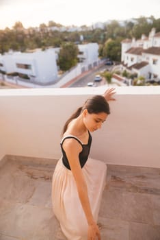 A dancer in a flowing dress captivates with art at sunset on a serene balcony overlooking vibrant scenery