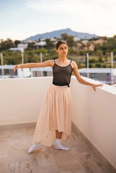 A graceful ballerina performs a stunning pose on a sunlit terrace with majestic mountains in the background
