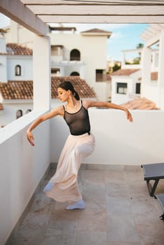 A talented dancer beautifully showcases her grace and elegance on a sunlit balcony, framed by stunning architecture