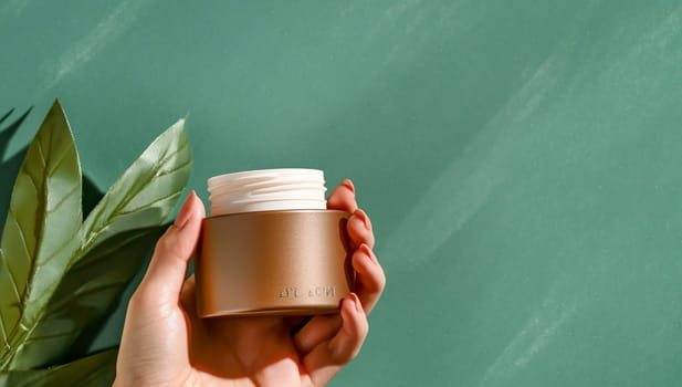 Hand model elegantly holds a luxurious cosmetic cream jar against a lush green background, perfect for showcasing beauty products. The serene setting adds natural elegance, ideal for skincare ads