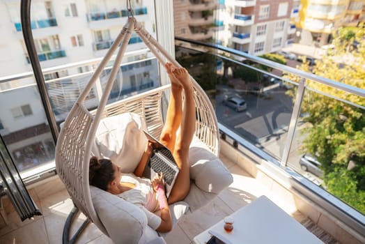 A person finds relaxation in a hammock on a beautifully sunlit balcony while working diligently on a laptop