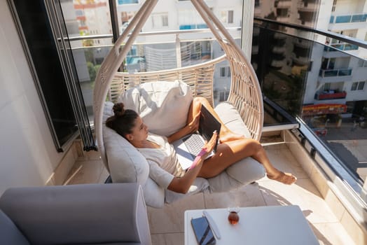 A woman enjoys her time on a balcony, reading on a tablet while relaxing in a stylish hanging chair