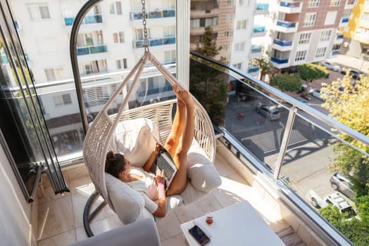 A person relaxes in a hanging chair on their balcony, enjoying the peaceful warmth of the morning sun