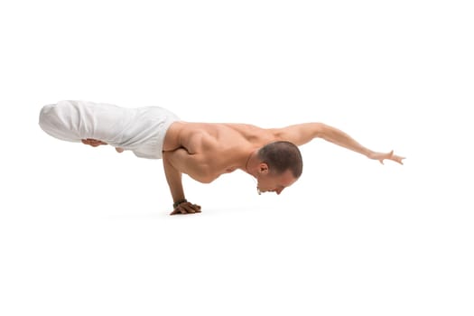 Mature shirtless muscular man wearing wide trousers practising yoga routine isolated on white
