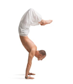 Mature shirtless muscular man wearing wide trousers doing yoga handstand isolated on white
