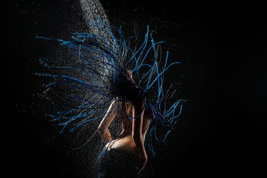 Brunette with blue dreadlocks topless having shower against black wall rearview shoot