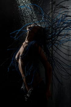 Brunette with blue dreadlocks topless having shower against black wall