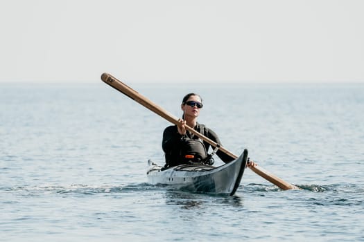 A woman in a black wetsuit paddles a kayak with a wooden paddle on calm water.