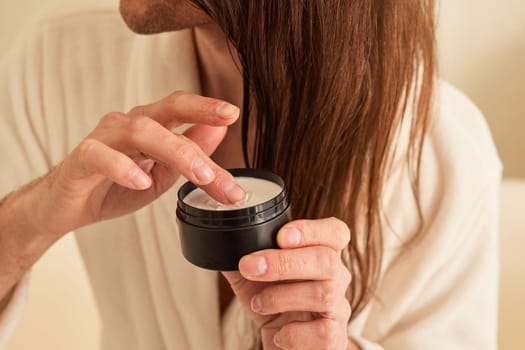 man with long hair takes white cream from black jar with finger close-up, daily body care for men