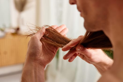 Hair care concept for men. A young guy looks at the ends of his hair close-up, hair loss