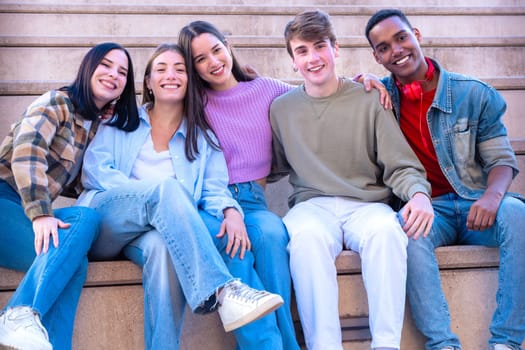 Five multiracial friends smiling and looking at the camera with cheerful expressions. Enthusiastic young people gathered