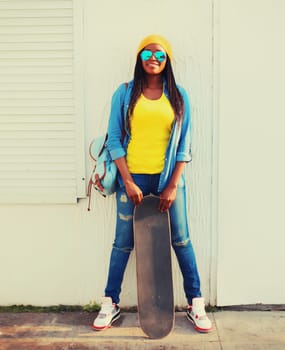 Stylish modern happy smiling young african american woman with skateboard in the city