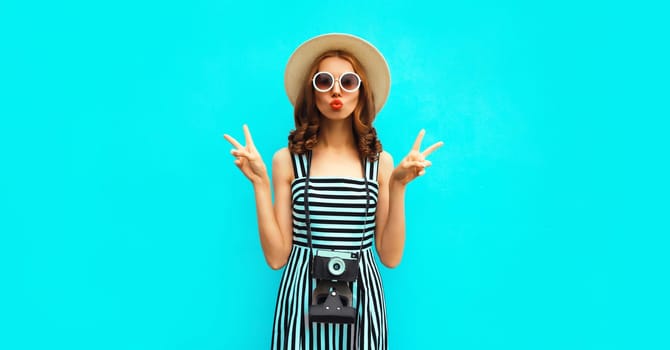 Summer portrait of happy smiling young woman photographer with vintage film camera wearing straw hat, dress, sunglasses on blue background