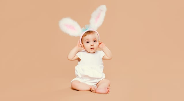 Portrait of cute baby with easter rabbit ears sitting on brown studio background