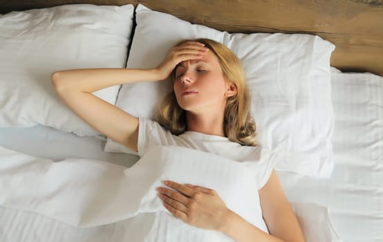 Upset exhausted woman with headache, pain tension in the head, suffers from migraine lying on the bed on pillow in bedroom at home