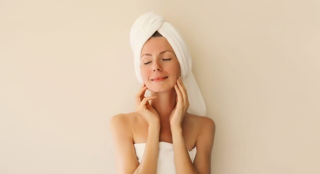 Natural beauty portrait of happy smiling young caucasian woman touches her clean skin while drying wet hair with white bath towel on her head
