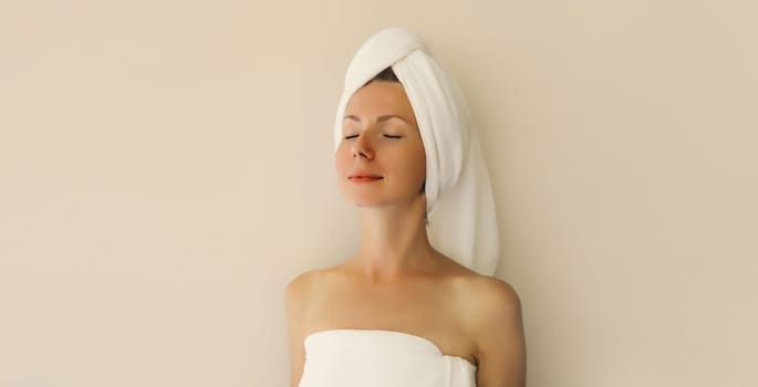 Natural beauty portrait of happy young caucasian woman enjoying her clean skin drying wet hair with white bath towel on her head