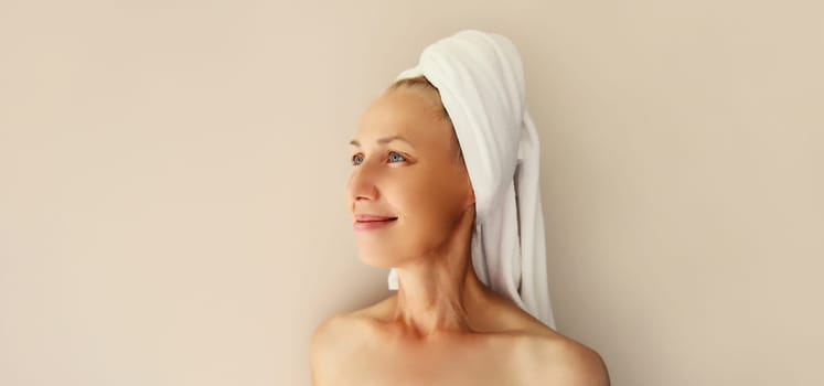 Natural beauty portrait of happy caucasian mature woman enjoying while drying wet hair with white bath towel on her head after shower in the morning at home