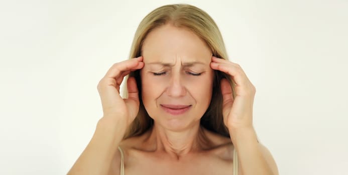 Exhausted tired mature woman touching head, suffering from headache, stress, fatigue, temples pain, migraine, loud noise, tension on white background