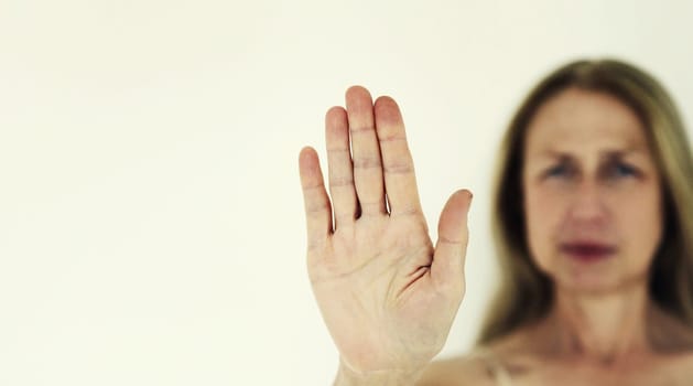 Upset woman shows stop, no or enough sign with palm of hand, refusal gesture, domestic violence.