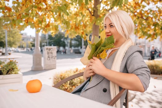 A woman sitting at a table with a leafy green plant in her hand.