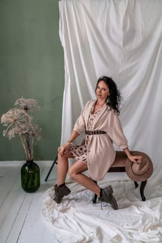 A woman is sitting on a bench in a room with a green wall. She is wearing a brown jacket and a hat