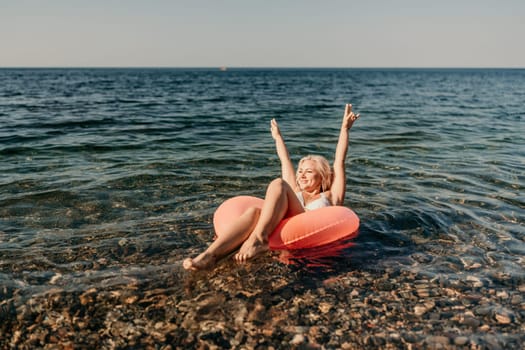 A woman is floating in the ocean on a red inflatable raft. She is smiling and she is having a great time. Concept of joy and relaxation, as the woman enjoys her time in the water