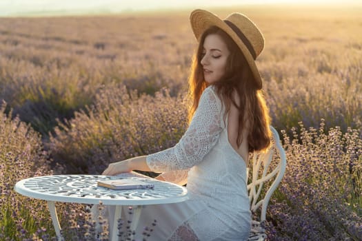 A woman wearing a straw hat is sitting in a field. She is smiling and she is enjoying the moment