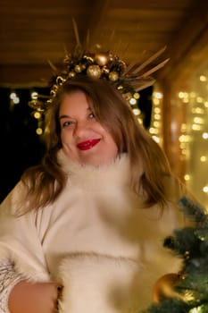 A woman with a festive crown of ornaments and branches smiles warmly. String lights twinkle in the background, suggesting a Christmas setting.