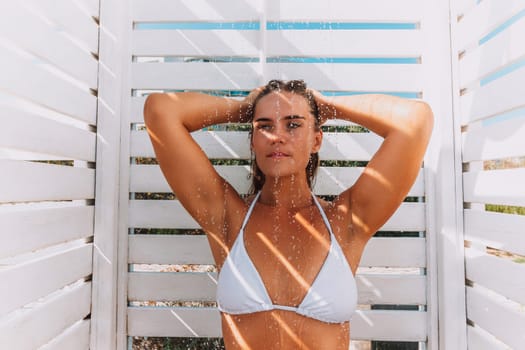 A woman is standing in front of a structure with a shower., with her arms raised and her hair blowing in the wind. She is enjoying the moment and taking in the beauty of her surrounding.
