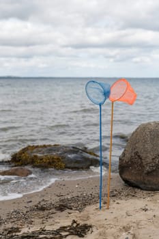 an orange and a blue fishing net on a pole standing on the beach with the sea and the horizon as a background in nature