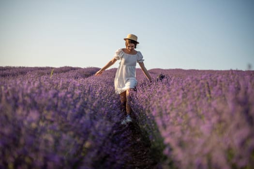 Lavender field happy girl in white dress with hat runs through a lilac field of lavender. Aromatherapy travel.