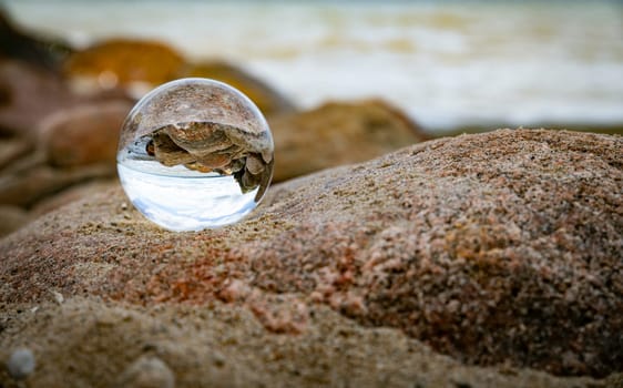 a glass ball with the reflection of rocks on the beach and the horizon and sky as a background