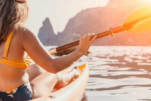 A woman paddles a kayak on a calm body of water, with rocky cliffs in the background.
