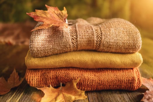 Stacked wool autumn sweaters on wooden background with leaves