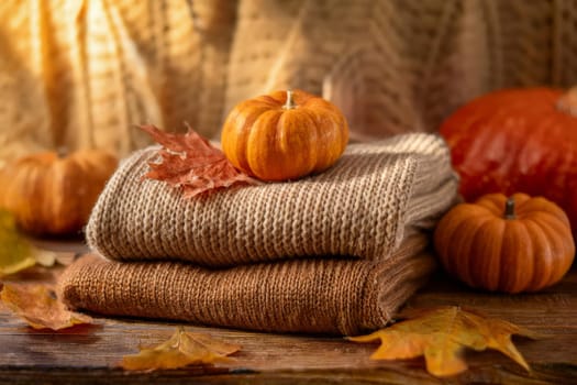 Stacked wool autumn sweaters on wooden background with leaves and pumpkins