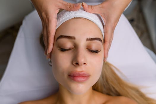 Portrait of pretty relaxed young woman lying with closed eyes having facial massage in spa salon. Female client enjoy receiving skin care procedure treatment. Wellness and beauty day concept. High quality photo