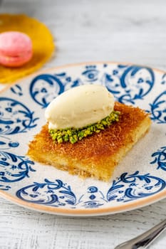 Kunefe with pistachios and ice cream on a porcelain plate on a wooden table