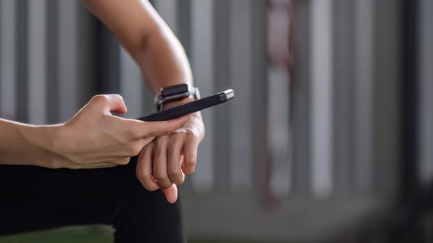 Young female athlete in sportswear sits at the gym using a cell phone while relaxing..