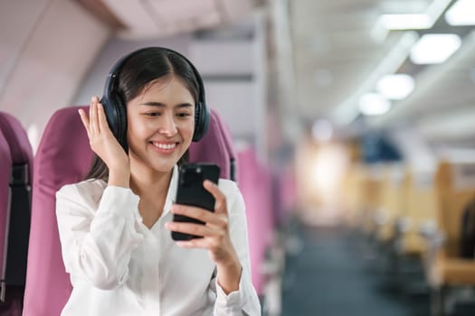 Asian woman sitting and using a smartphone in an airplane Listening to music next to the airplane seat window travel and technology concept.