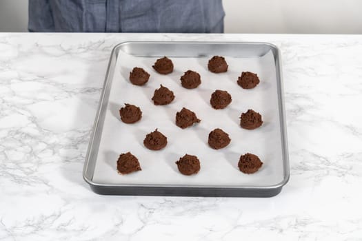 Scooping cookie dough with dough scoop into a baking sheet lined with parchment paper to bake chocolate cookies with chocolate hearts for Valentine's Day.