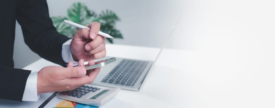 Businessman holding a pen and smartphone is working on a white table with a computer on it. On a white background with copy space.