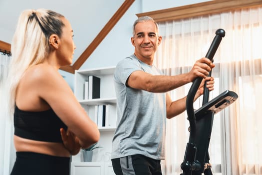 Active senior couple running on elliptical running machine at home together as fitness healthy lifestyle and body care after retirement for pensioner. Clout